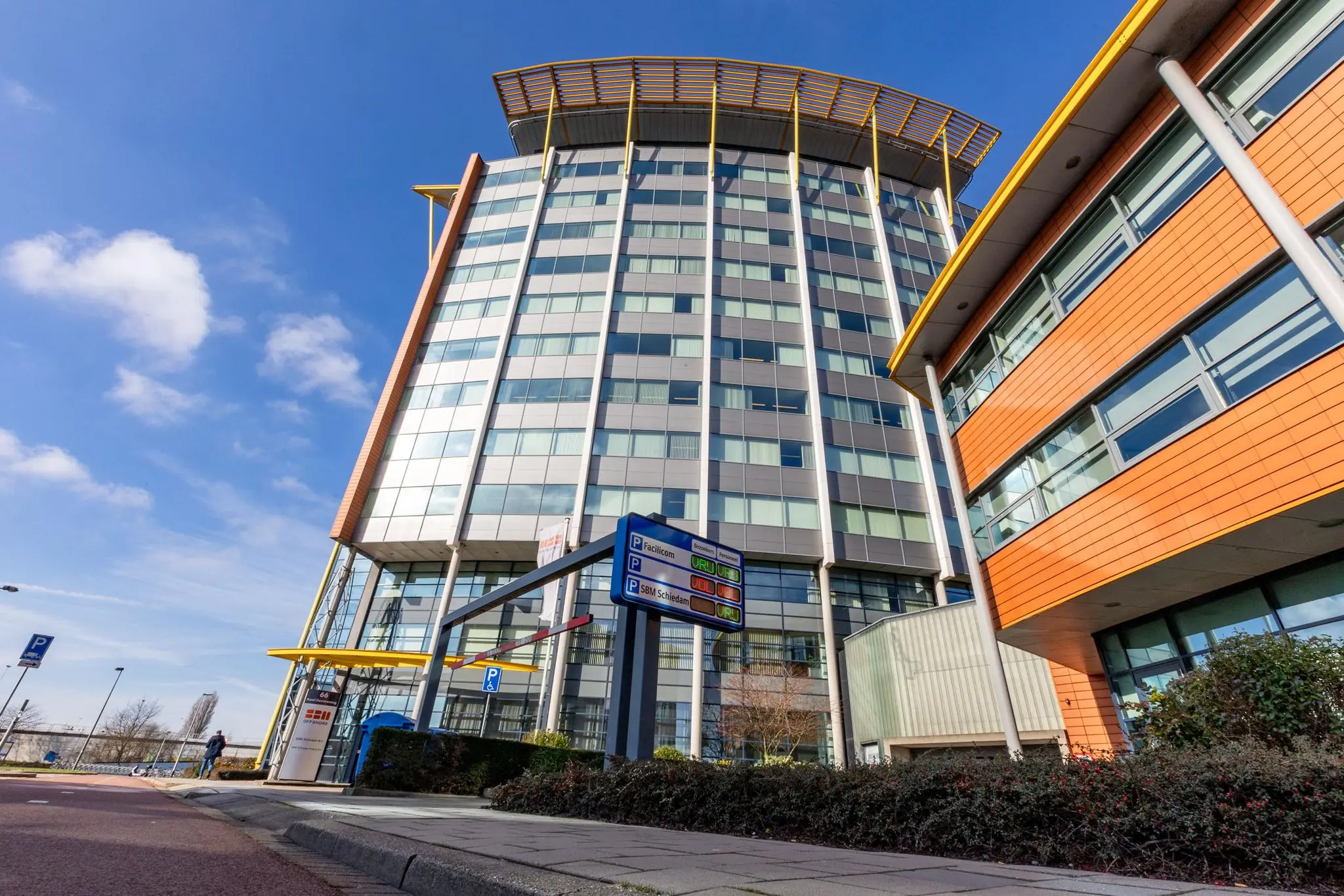 Hoog kantoorgebouw aan de Karel Doormanweg met moderne gevel en parkeeraanduiding op de voorgrond.